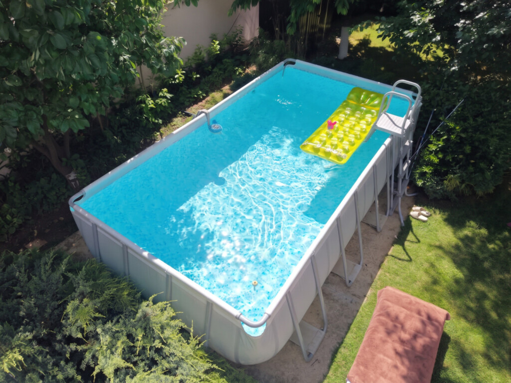 Drone view of the rectangular above-ground pool in the garden, with the bitumen roof of the tool shack that carries the solar loop in the corner of the frame