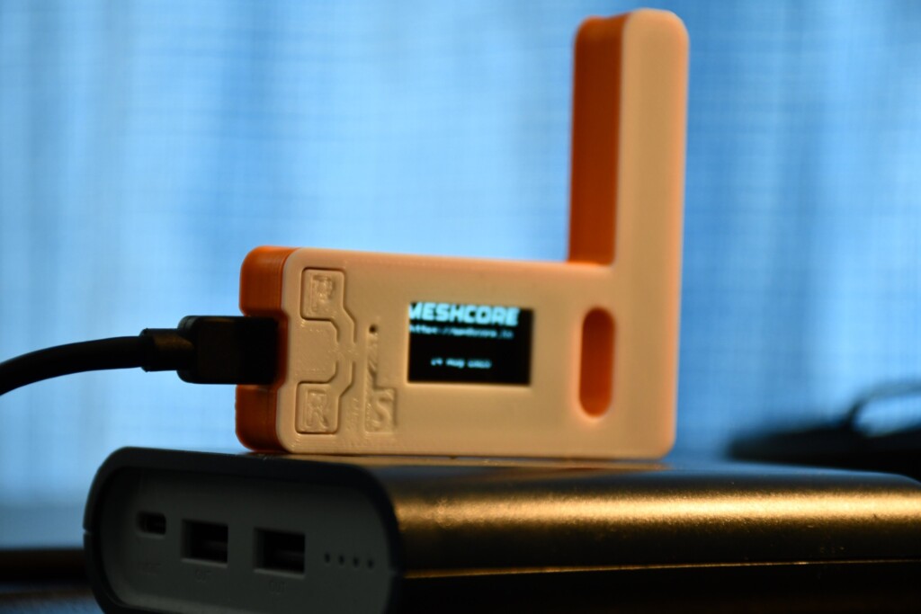 The TTGO LoRa32 V1.0 in its 3D printed case, the OLED showing the MeshCore boot screen